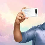 Man taking a selfie using Realme 16 5G smartphone with rear camera and selfie mirror feature against a colorful pastel background