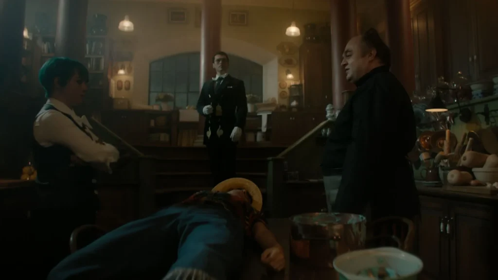 Live-action scene showing Luffy lying unconscious on a table surrounded by Klahadore, Sham, and Buchi in a dimly lit kitchen.