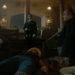 Live-action scene showing Luffy lying unconscious on a table surrounded by Klahadore, Sham, and Buchi in a dimly lit kitchen.