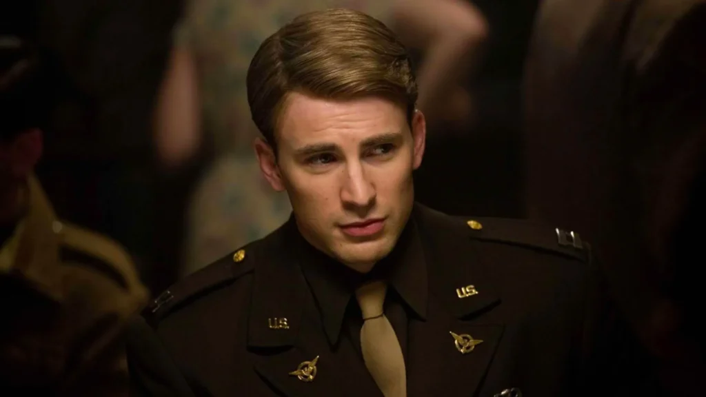 Chris Evans as Steve Rogers wearing a dark brown World War II military dress uniform with gold U.S. collar pins and a tie, looking thoughtfully to the side.