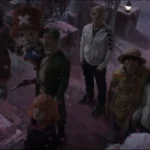 The Straw Hat Pirates and their allies stand together in a snowy courtyard beneath drifting pink cherry blossom snow, looking upward with hopeful expressions outside Drum Castle. Chopper stands at the center beside Luffy, while Zoro, Sanji, Nami, Usopp, and Vivi gather around during the emotional finale of One Piece live-action Season 2, Episode 8, "Deer and Loathing in Drum Kingdom."