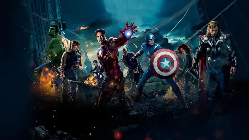 The Avengers team, including Iron Man, Captain America, Thor, Hulk, Black Widow, Hawkeye, and Nick Fury, standing combat-ready in a destroyed, burning city street.