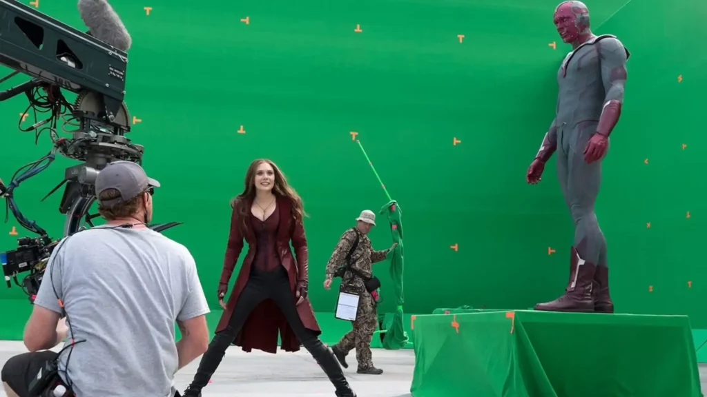 Behind-the-scenes set photo showing Elizabeth Olsen as Scarlet Witch posing in front of a giant green screen next to Vision.