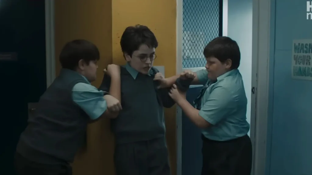 Dudley's gang cornering a young, dark-haired Harry Potter in glasses against a yellow wall in a school hallway.