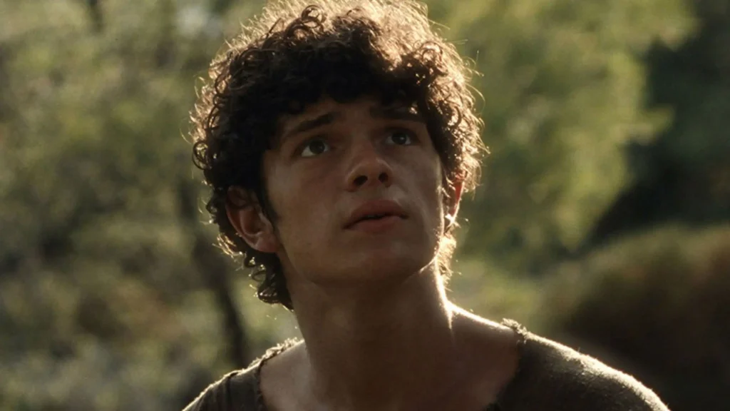Close-up shot of actor Noah Jupe with dark curly hair looking upward intently against a soft-focus, natural outdoor background.