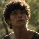 Close-up shot of actor Noah Jupe with dark curly hair looking upward intently against a soft-focus, natural outdoor background.