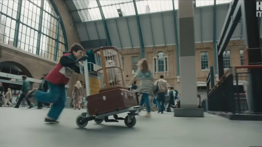 Young Harry Potter pushing a luggage cart with Hedwig's cage, running fast toward a brick column at King's Cross Station.