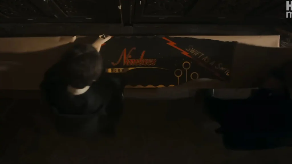 Top-down view looking into a long wooden box containing a brand-new Nimbus 2000 broom wrapping with text reading "Swift as a Snitch".