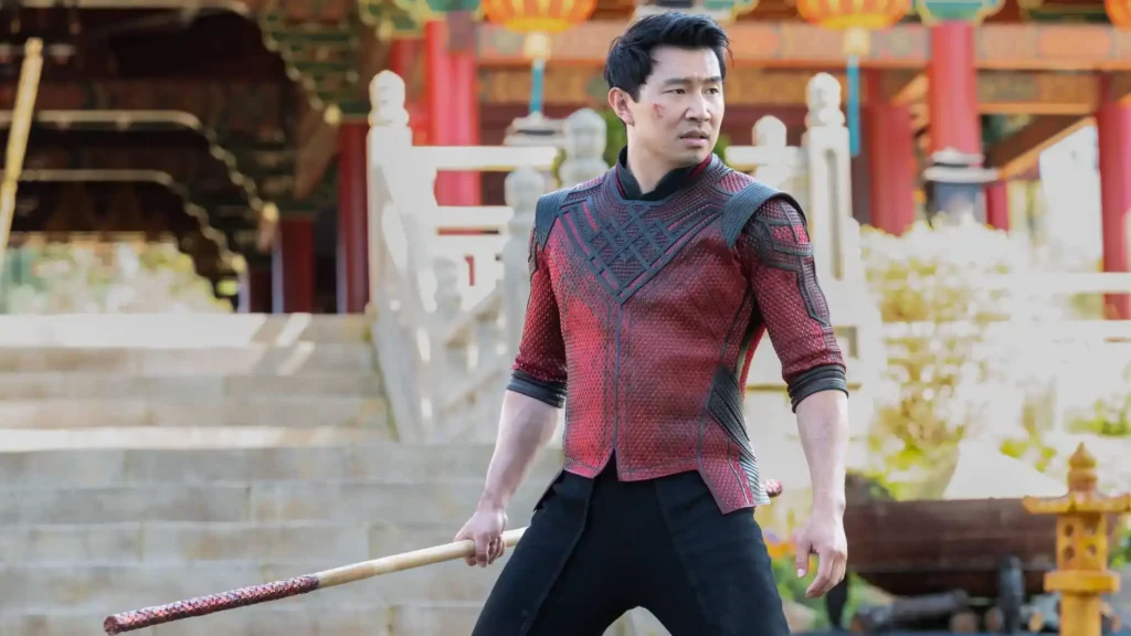 Simu Liu as Shang-Chi holding a bo staff while wearing his red and black armor in Ta Lo.