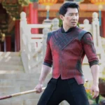 Simu Liu as Shang-Chi holding a bo staff while wearing his red and black armor in Ta Lo.