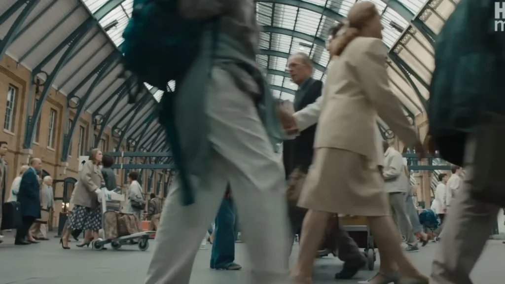 Muggle commuters in early 1990s vintage clothing walking past Petunia Dursley wearing large retro glasses.