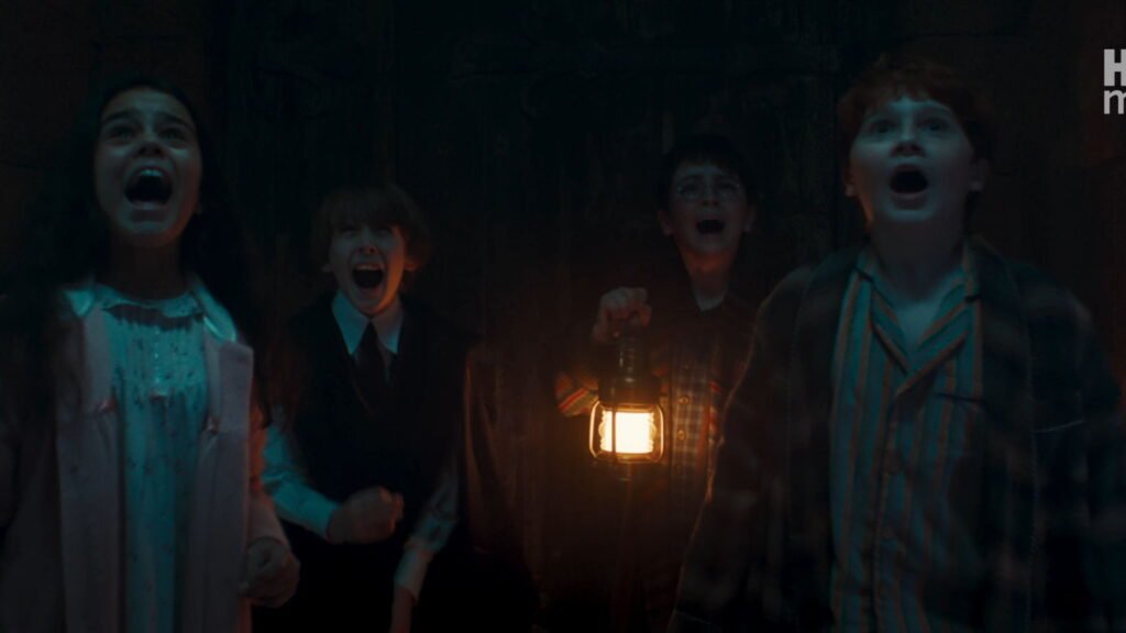 Hermione, Neville, Harry holding a lantern, and Ron gasping in fear inside a dark Hogwarts corridor.
