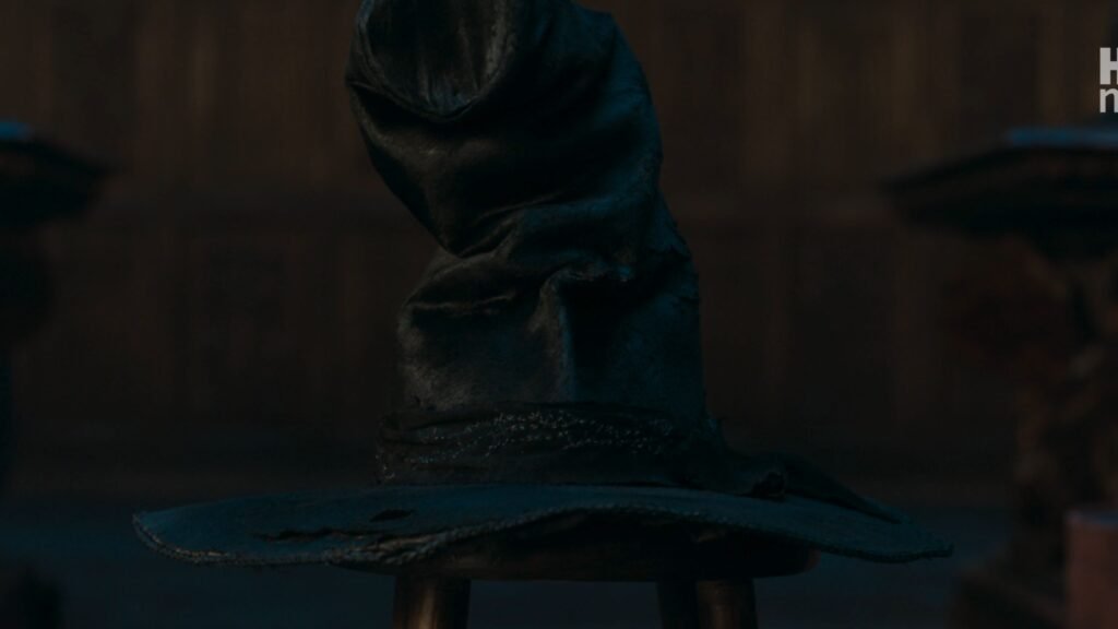 Close-up of the weathered, dark leather Sorting Hat resting on a wooden stool in a dimly lit room.